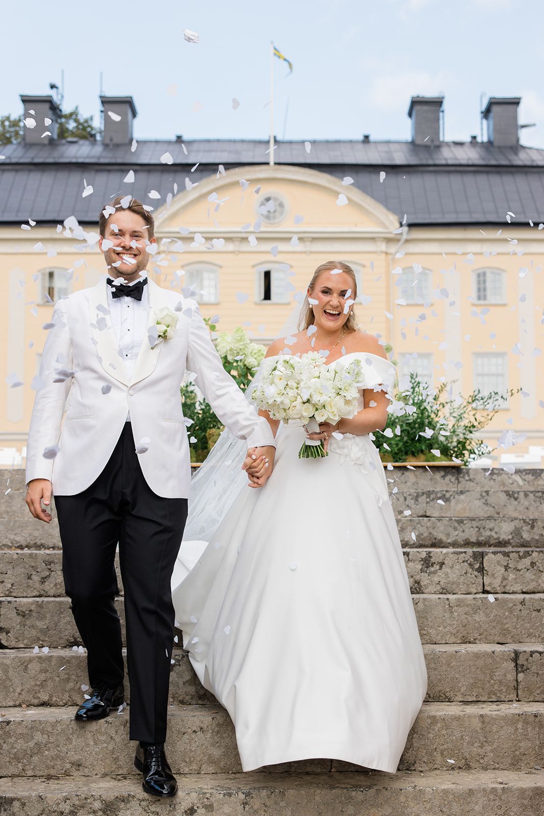 Couple embraces in front of dark wooden door as white petals fall.
