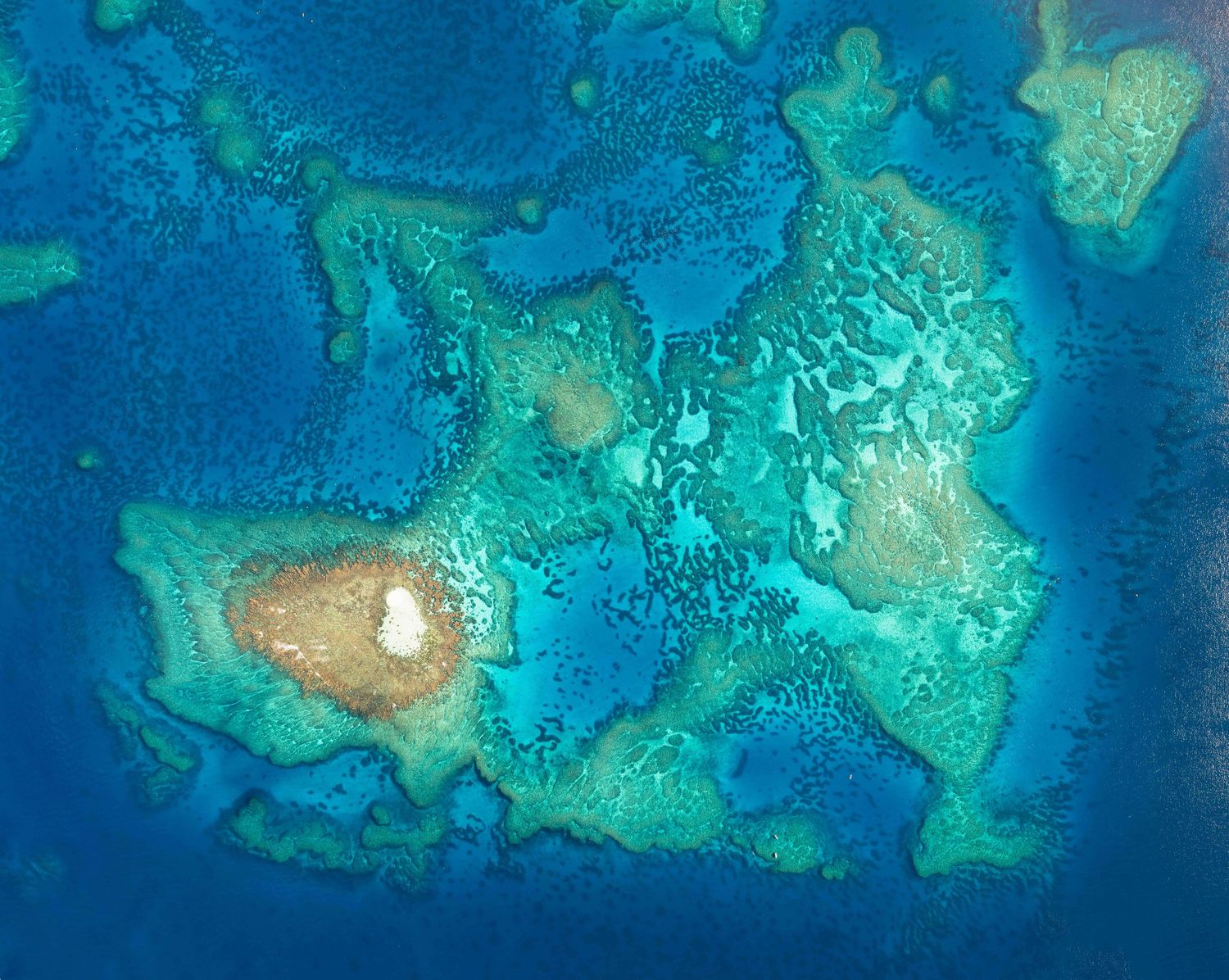 Aerial view of turquoise coral reefs and sandy patches in clear tropical waters of the Great Barrier Reef.