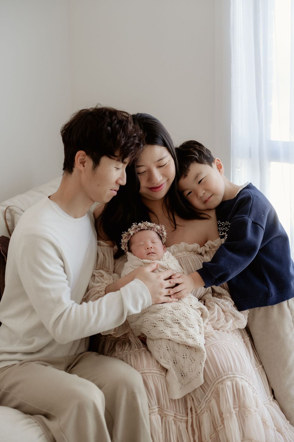 A loving family of four admires their newborn baby during a soft, natural light portrait session.