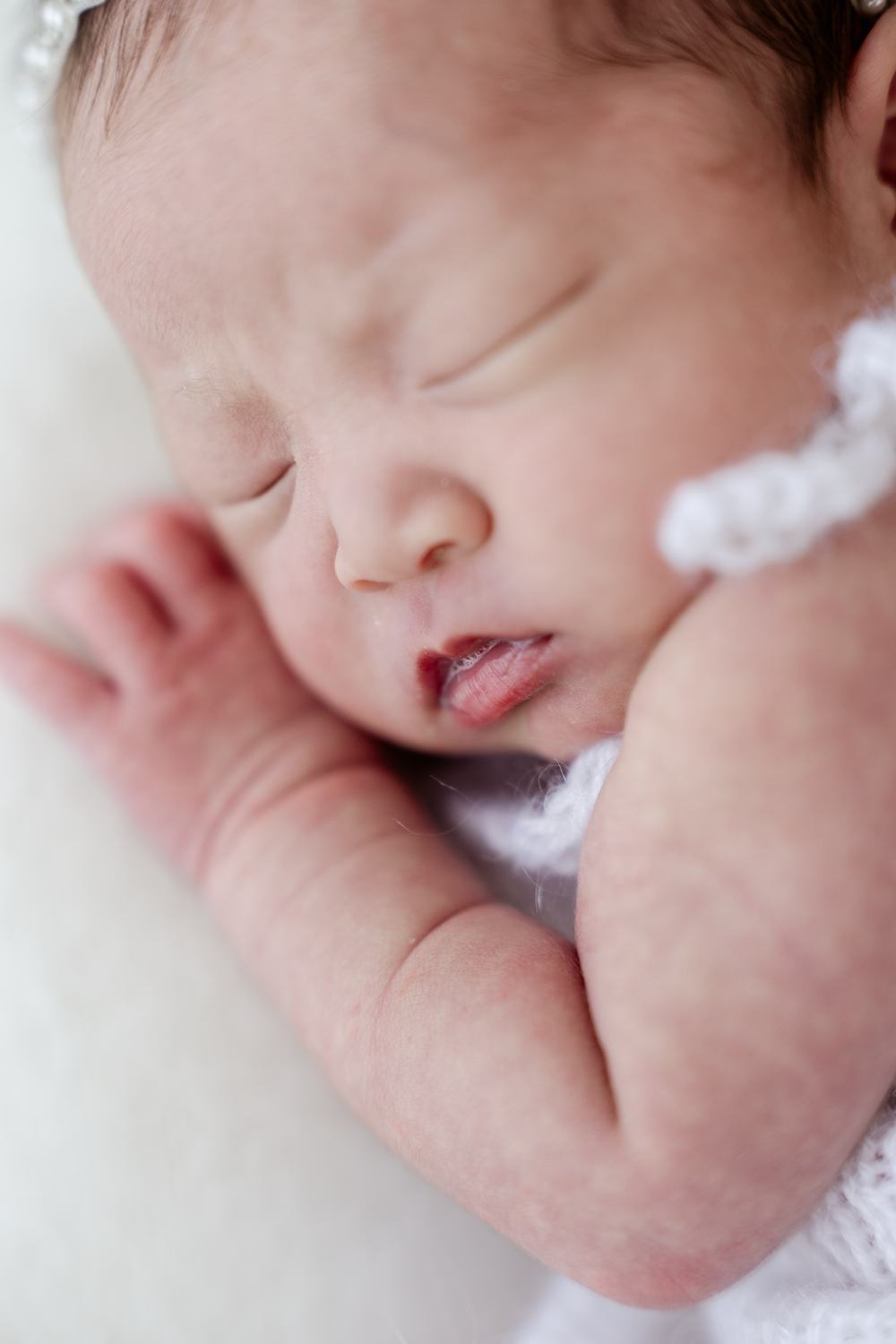 Peaceful sleeping newborn baby in white crochet outfit, close-up portrait of infant with tiny hands and delicate features.