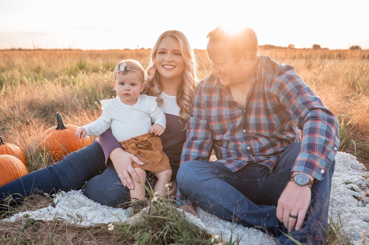 Family portrait featuring a mother, father, and a child sitting together in a grassy field Palm Bay Melbourne Brevard County Florida