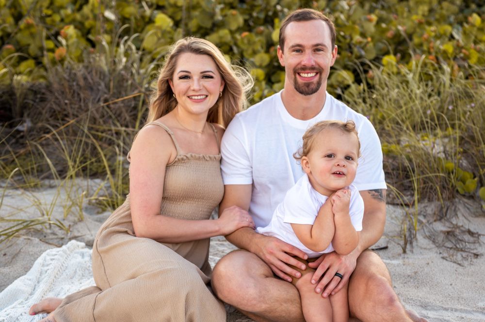 Family portrait featuring a smiling mother, father, and a child sitting together on beach Palm Bay Melbourne Cocoa Beach Vero Beach Florida