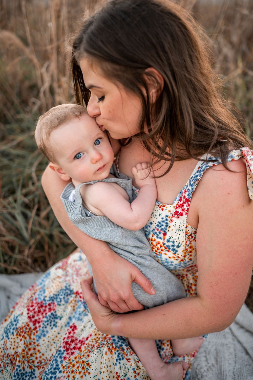 Mother kissing her baby in her lap sitting in field grass candid moment Mommy and Me Photoshoot Melbourne Cocoa Beach Brevard County Florida
