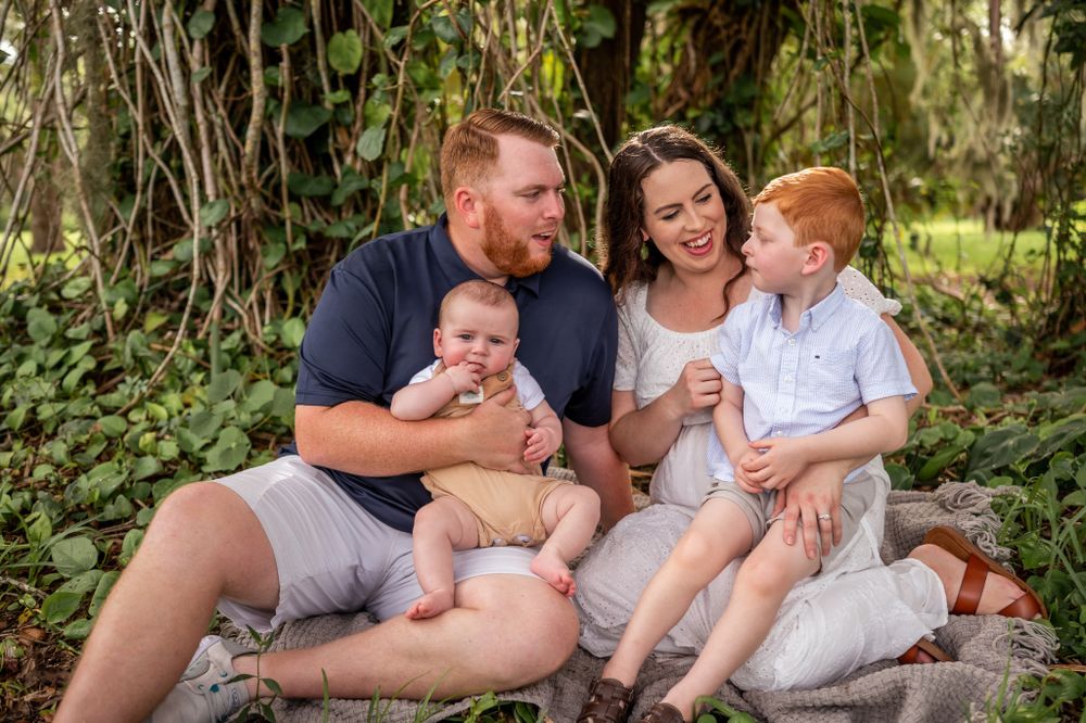 Family portrait featuring a mother, father, and two children sitting together park trees greenery Melbourne Palm Bay Brevard County Florida