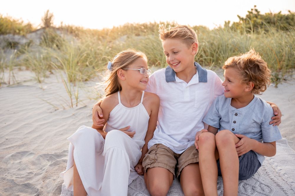 Three children sitting in the sand at the beach smiling at each other family photoshoot session Melbourne Cocoa Vero Florida Brevard County