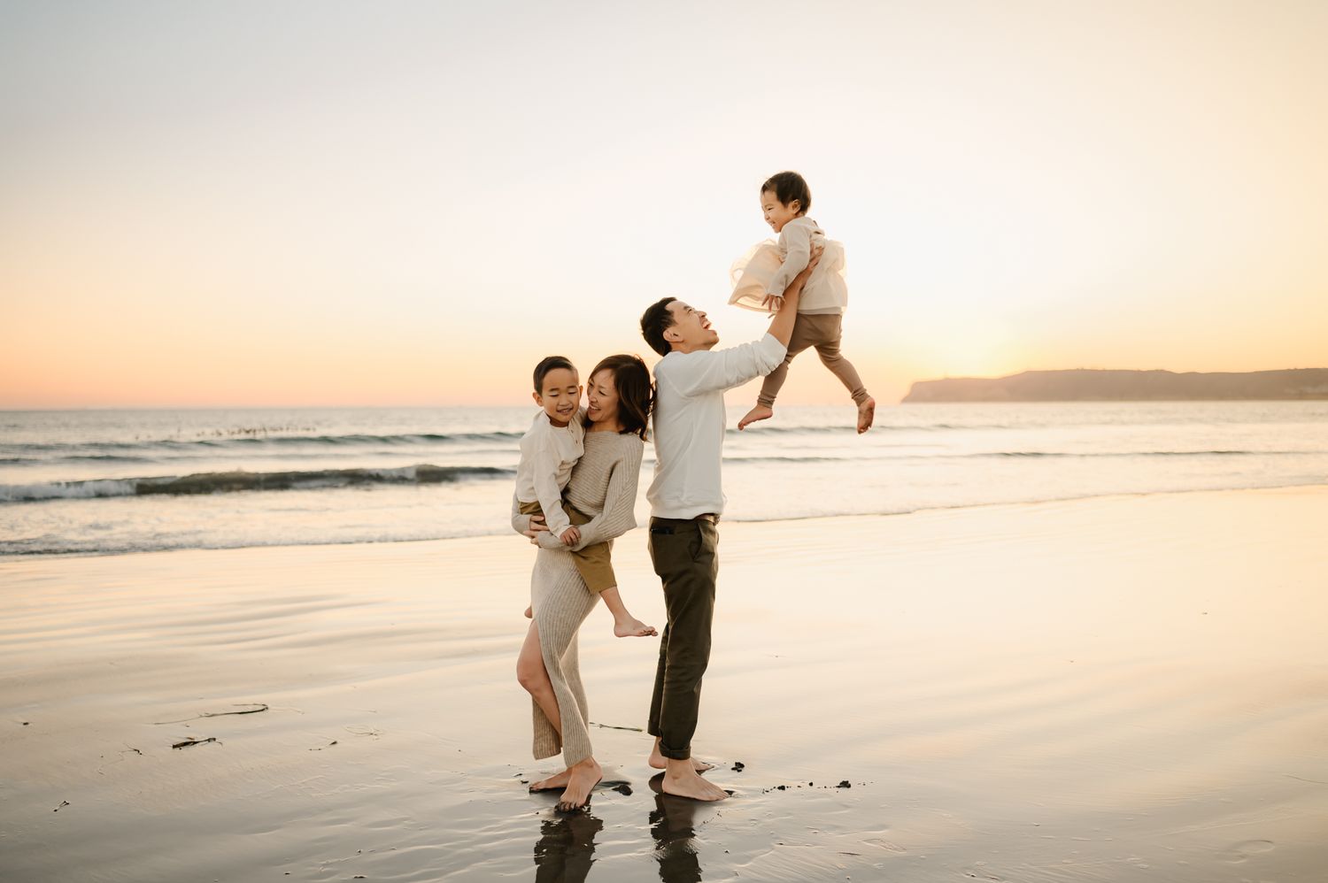 Family of four playing with their two young children on Coronado Beach during sunset. by Ventura family photographer