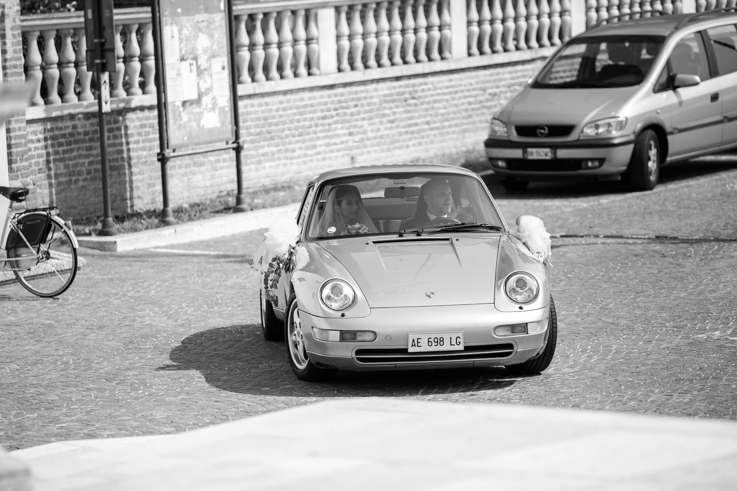 Vintage cars parked along a white stone balustrade outside a church.