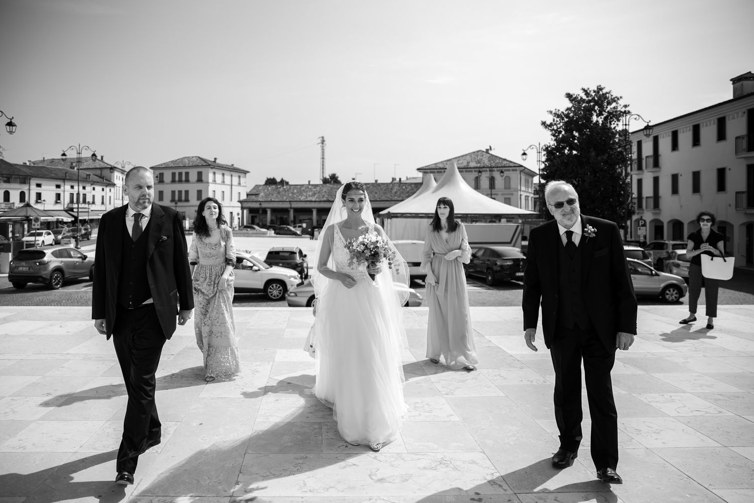 Wedding party walks together in black and white photograph on city street.