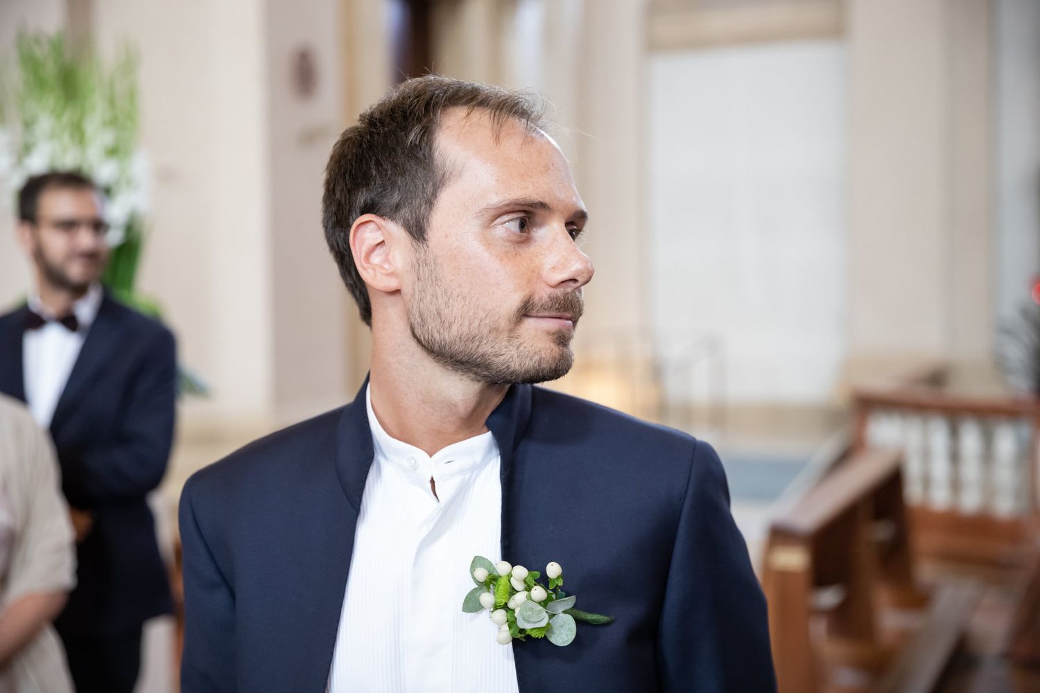 Groom in navy suit with boutonniere stands in formal attire.