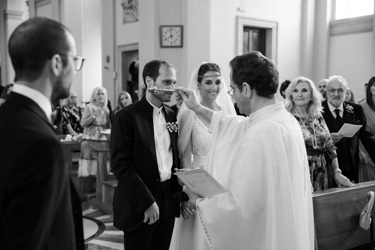 Wedding ceremony with priest and attendees in church setting.