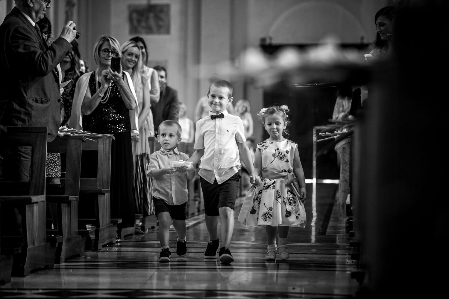 Children walking down church aisle during wedding ceremony in black and white.