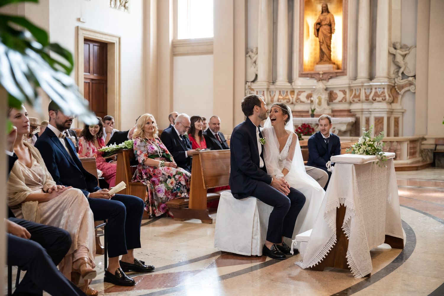 Wedding couple seated during church ceremony with guests in pews.