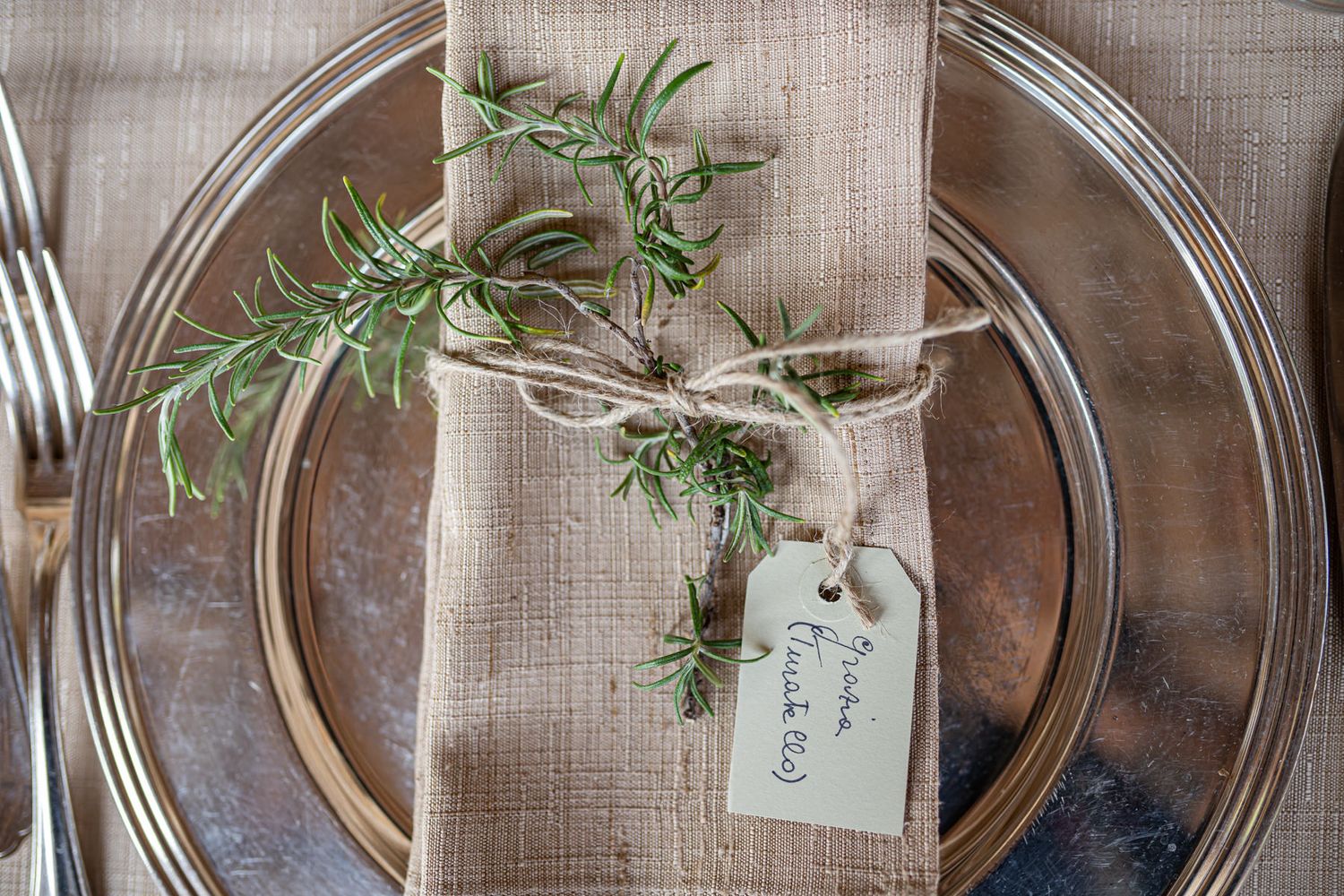 Place settings with fresh herbs and name cards on natural linen tablecloths.