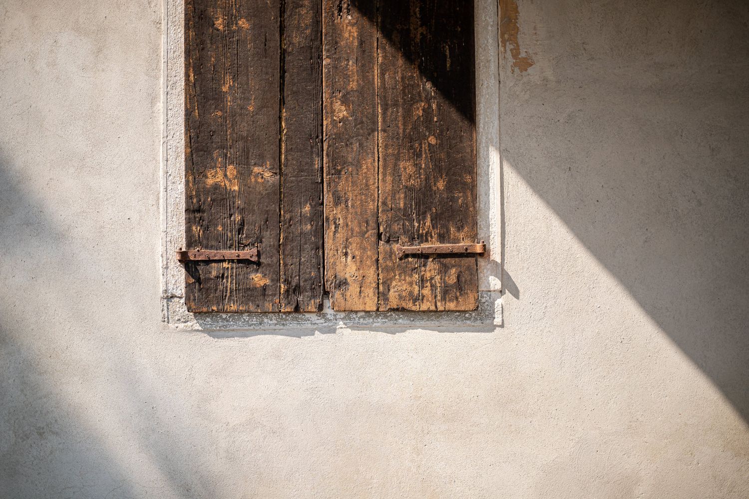 Rustic wooden shutters casting dramatic shadows on a weathered stone wall.
