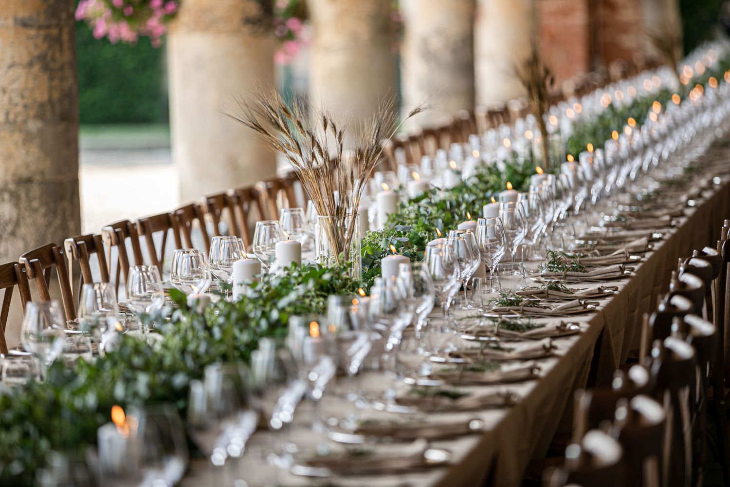 Long elegant wedding reception table setup with white linens and floral arrangements under a covered outdoor space.