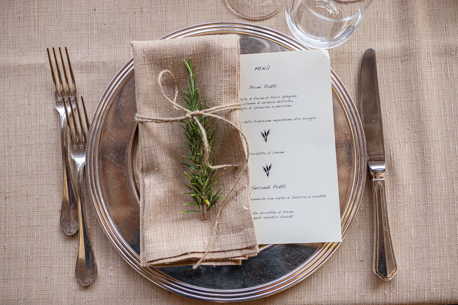 Place settings with silverware, menu cards and greenery sprigs on natural linen tablecloths.