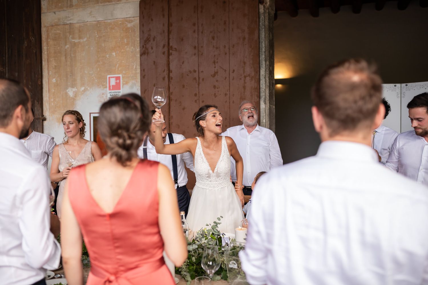 Wedding reception guests mingling in a rustic stone venue with coral bridesmaid dresses.