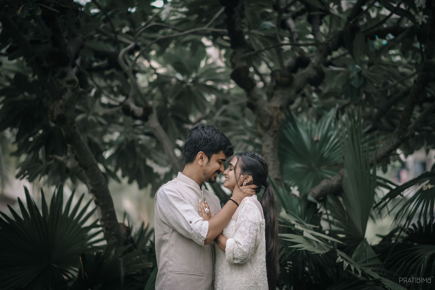A couple sharing an intimate moment in a lush tropical garden setting.