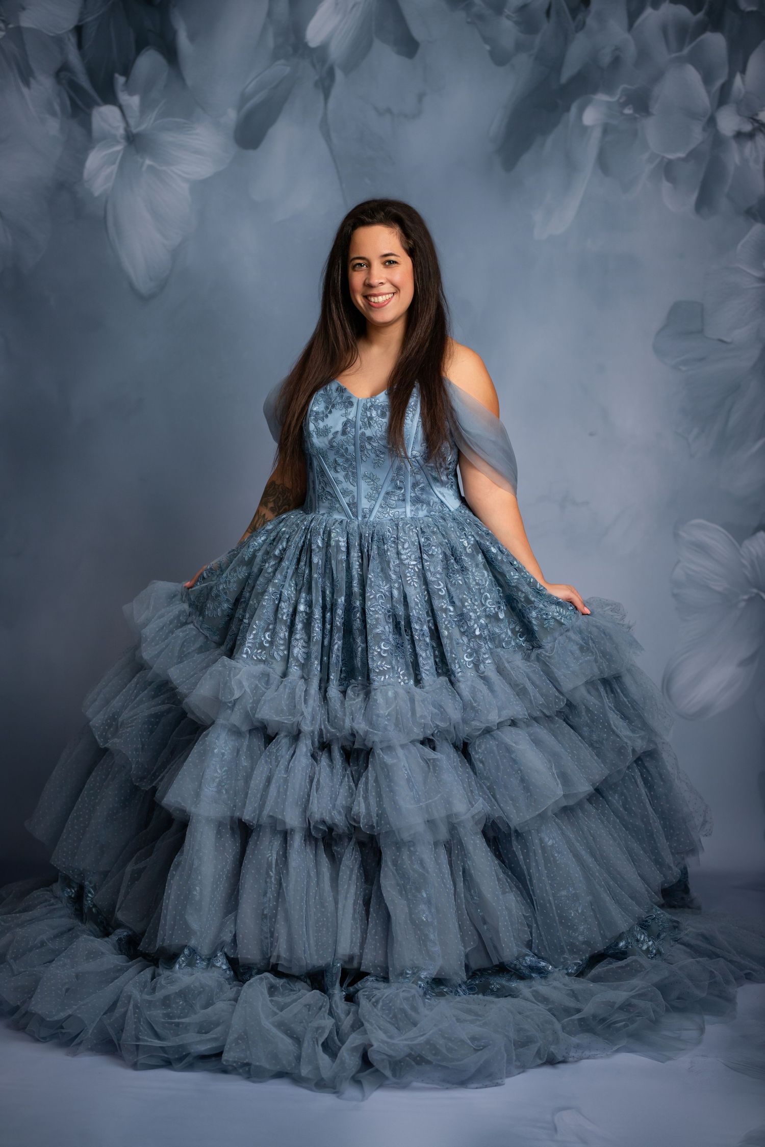 Ethereal portrait in flowing ice blue layered tulle gown with floral details against pale backdrop.
