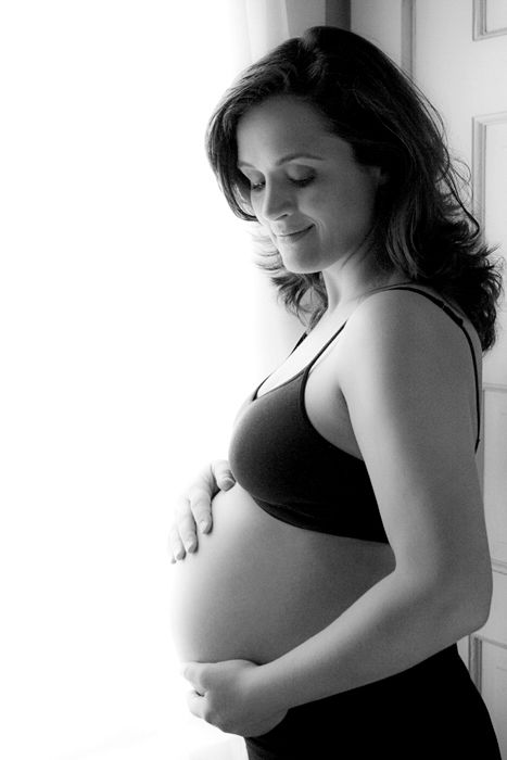 Black and white portrait of an expectant mother in profile, gently touching her baby bump.