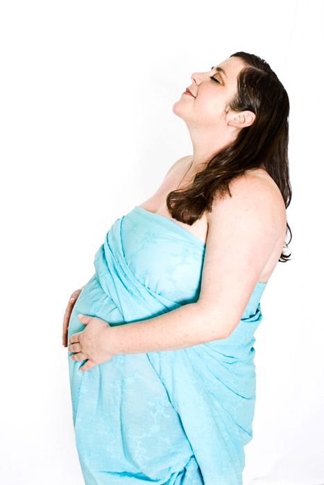 An expectant mother wrapped in blue fabric poses joyfully against white background.