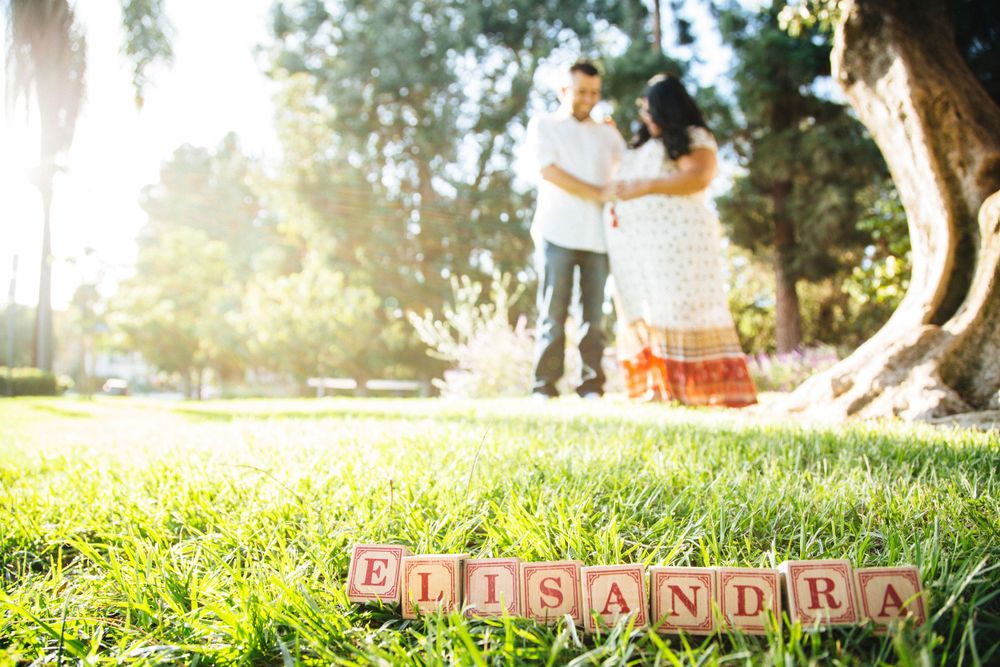 Baby name blocks spelling out a name on grass with a couple in the blurred background.