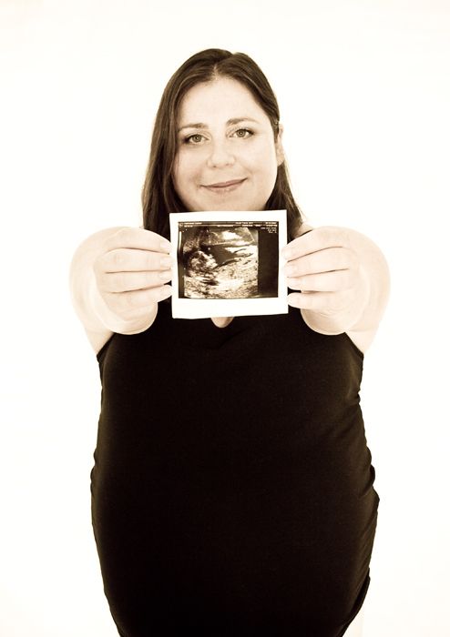Expectant parent holding up ultrasound photo wearing dark clothing.