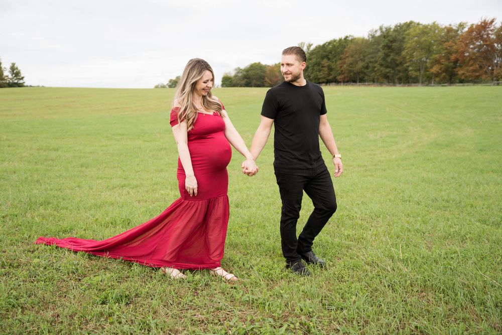 Candid maternity moment captured while walking through a green meadow.