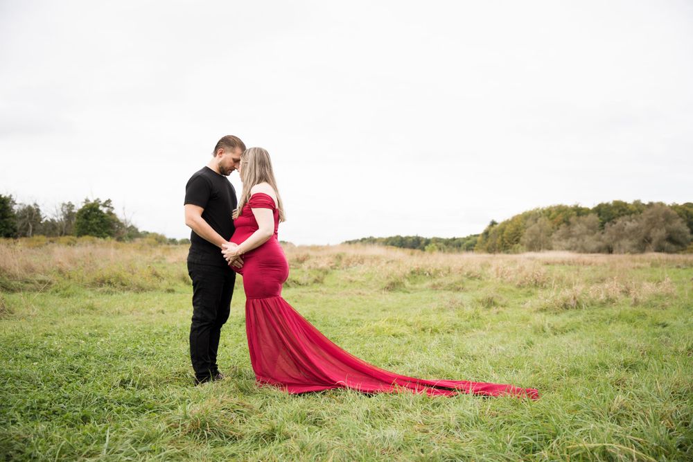 Dramatic maternity photo with flowing red dress in an open field.