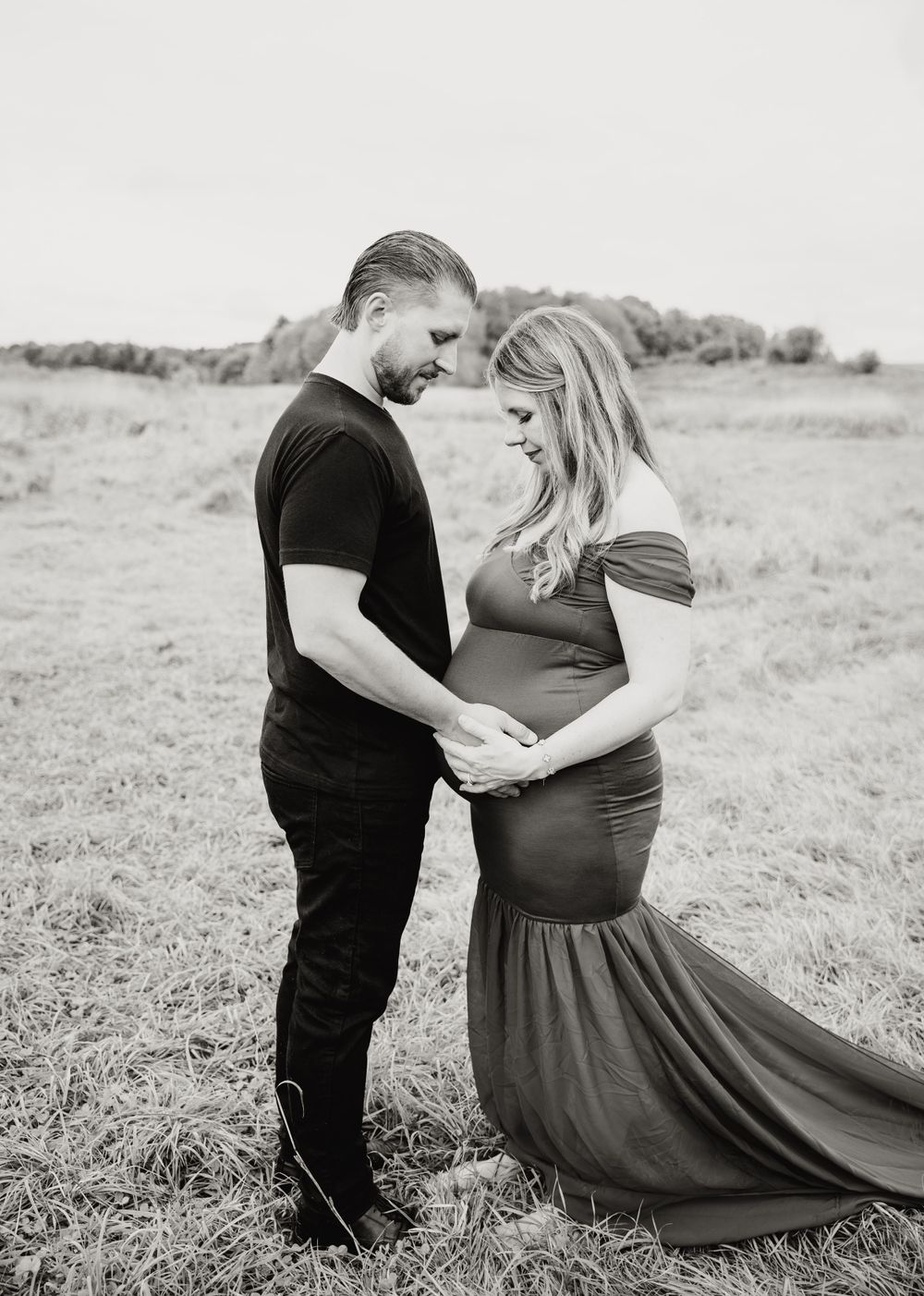 Black and white maternity portrait showing intimate moment in rustic field setting.