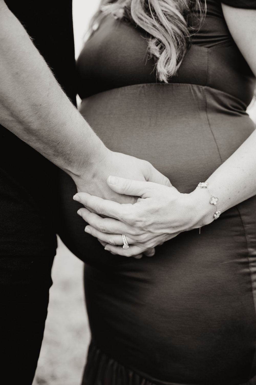 Black and white close-up of hands tenderly placed on pregnant belly.