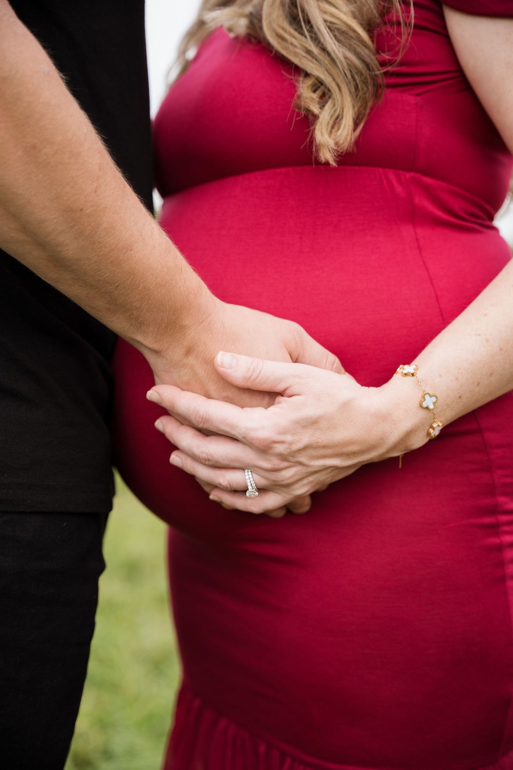 Close-up of hands resting on baby bump in red maternity dress.