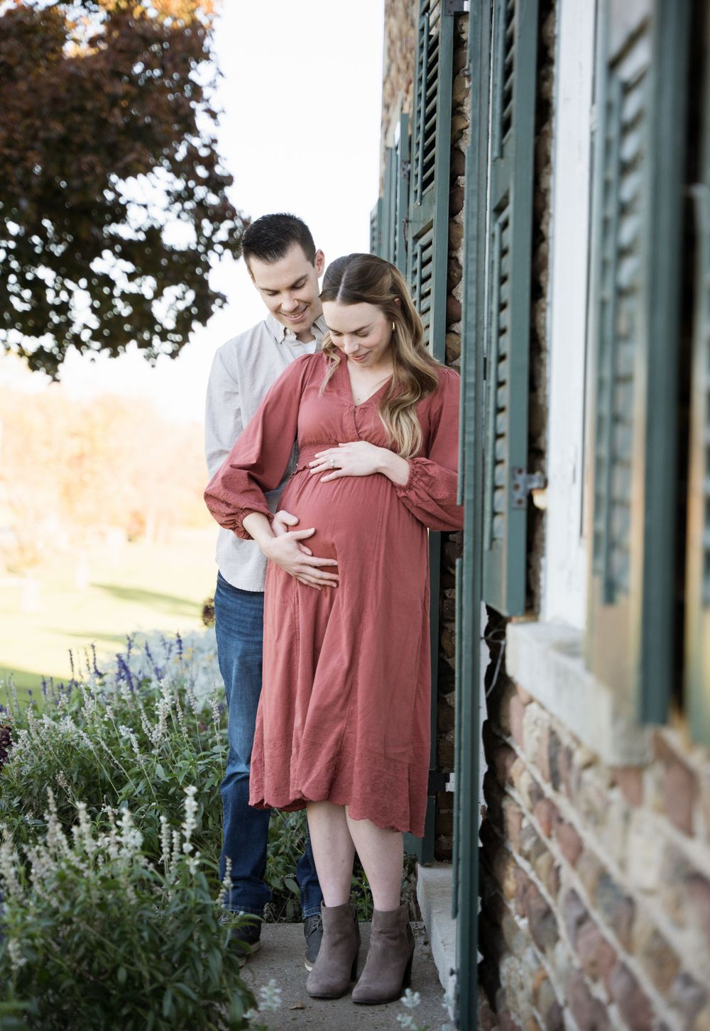 Couple shares tender moment by historic building with green shutters during maternity photoshoot.