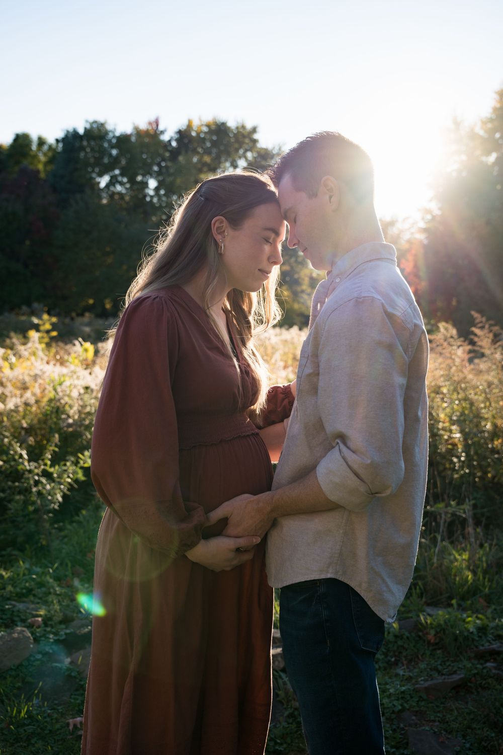 Romantic sunset maternity photo capturing a gentle moment between couple in a wildflower field.