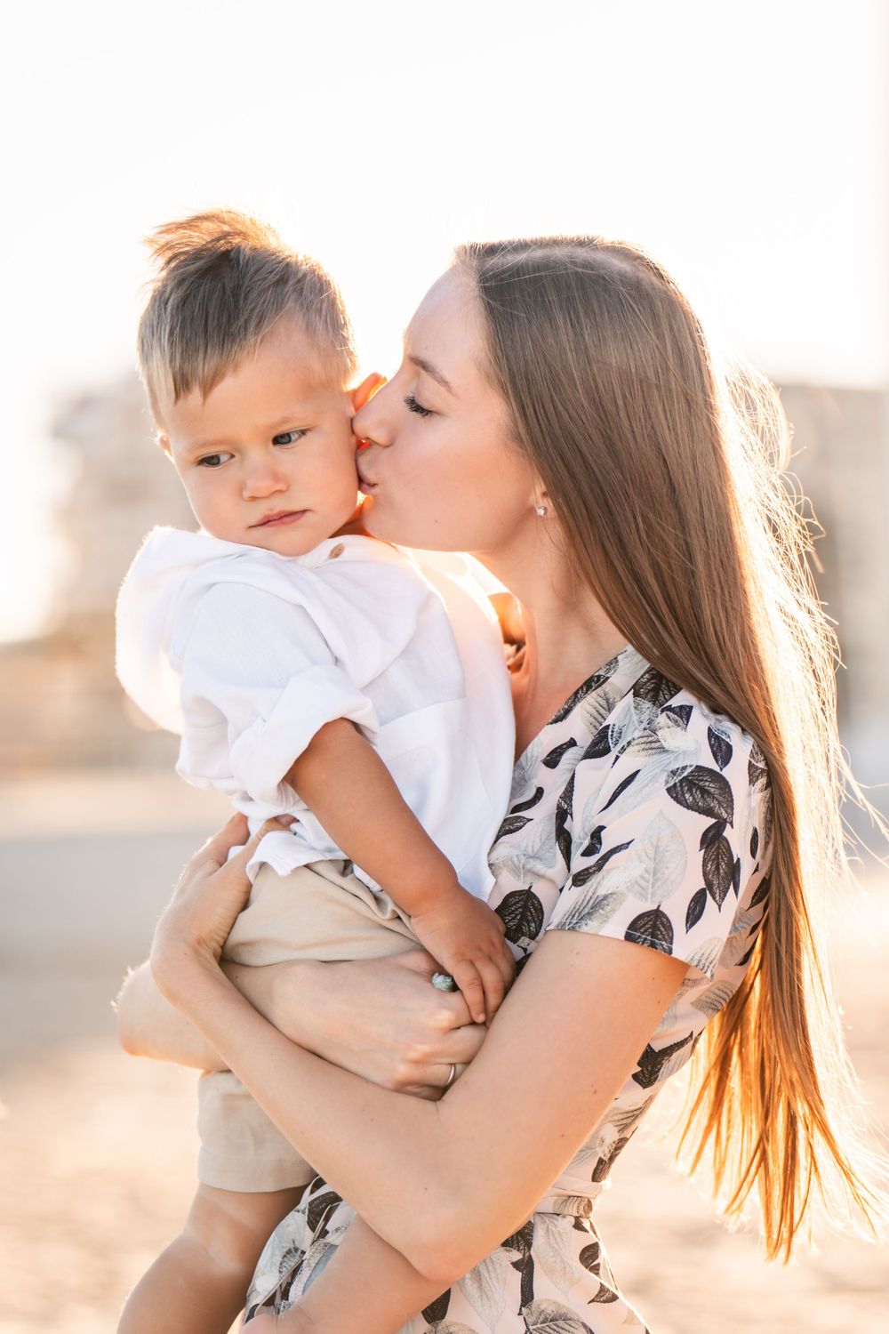 mother holding and kissing young son at sunset on the beach in alicante