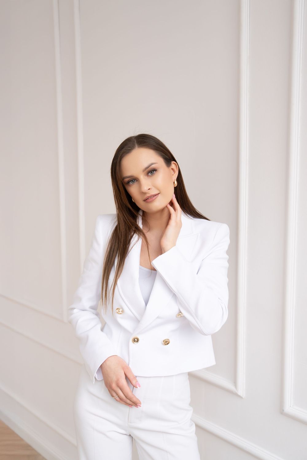 Professional model in crisp white suit poses against classic wall paneling.