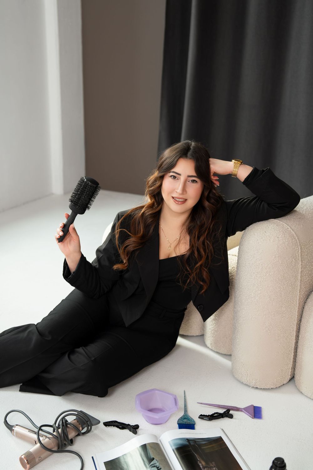 Professional hairstylist relaxing on couch with styling tools and hair accessories displayed on white surface.
