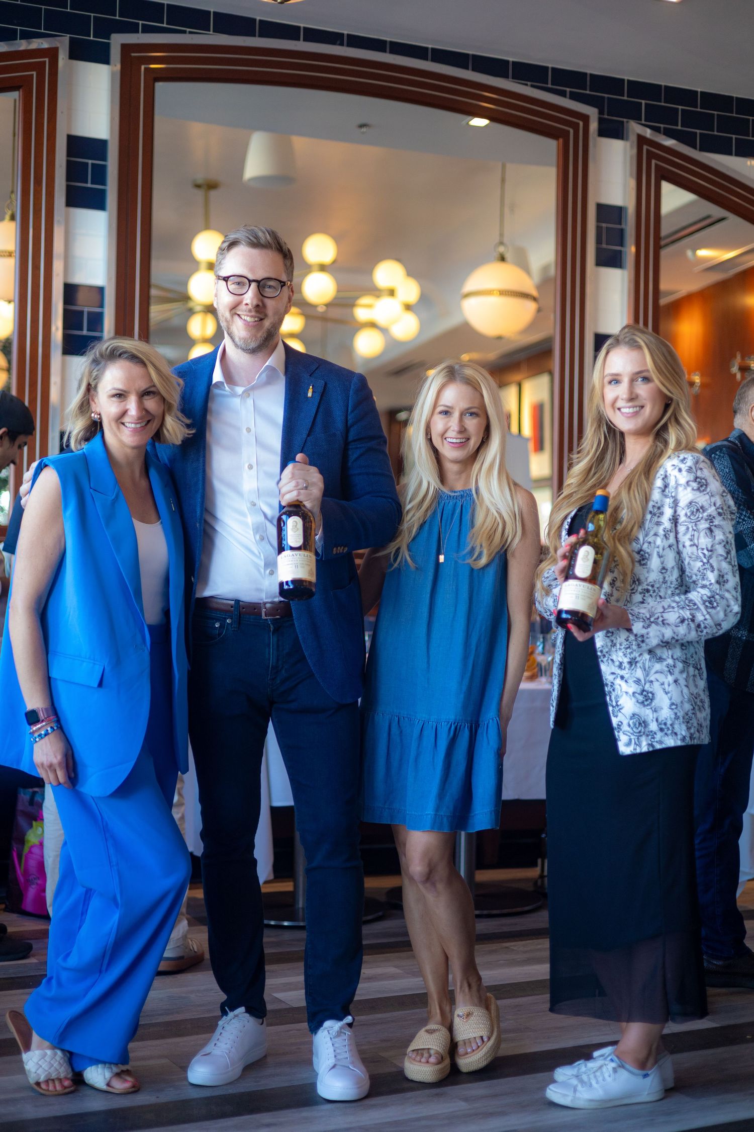 Four people in business attire holding wine bottles at an upscale restaurant entrance.