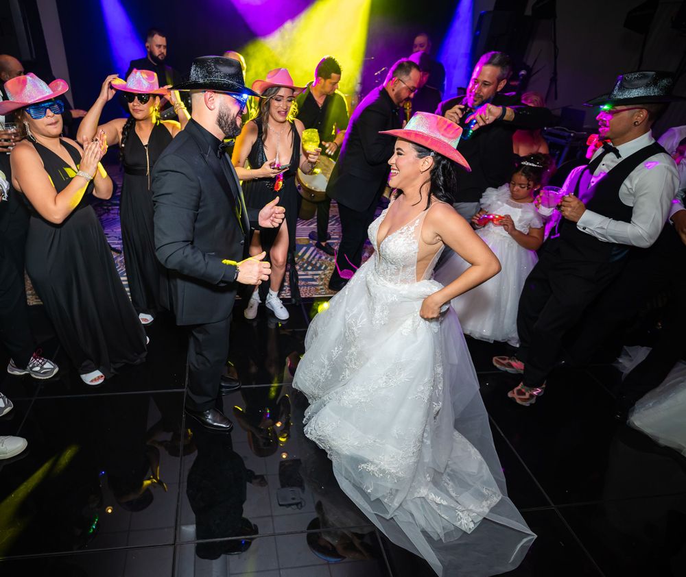 Wedding reception dance party with guests wearing cowboy hats under colorful lighting.