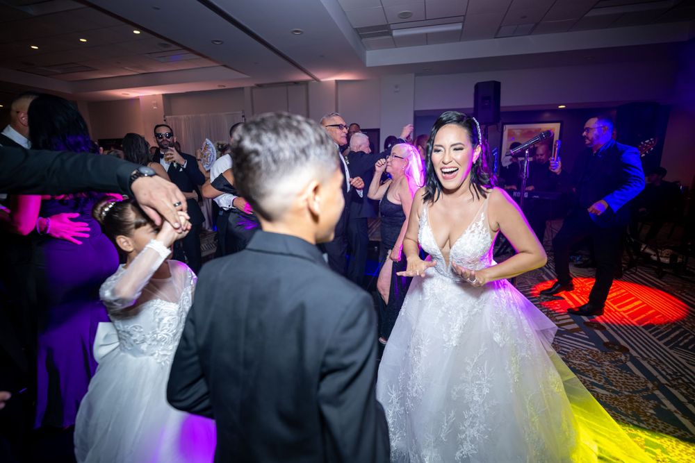Bride in white gown dances under vibrant purple and red lighting at wedding reception.