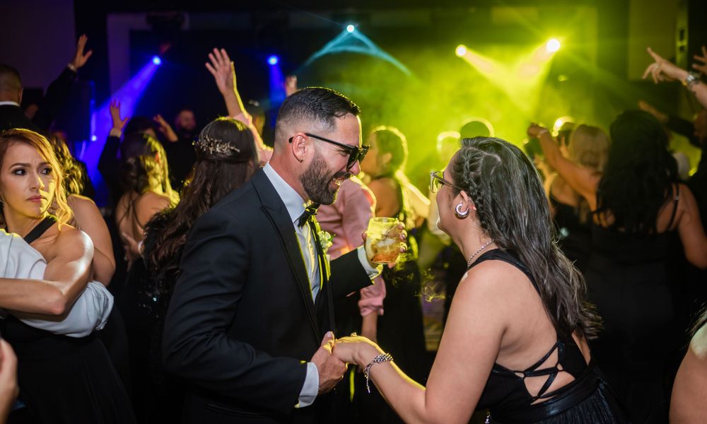 Wedding guests dancing on a darkened dance floor illuminated by colorful spotlights.