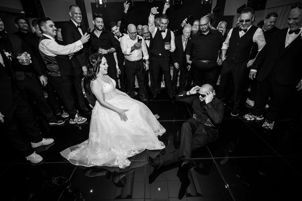 Black and white photo of wedding party dancing at reception with dramatic lighting.