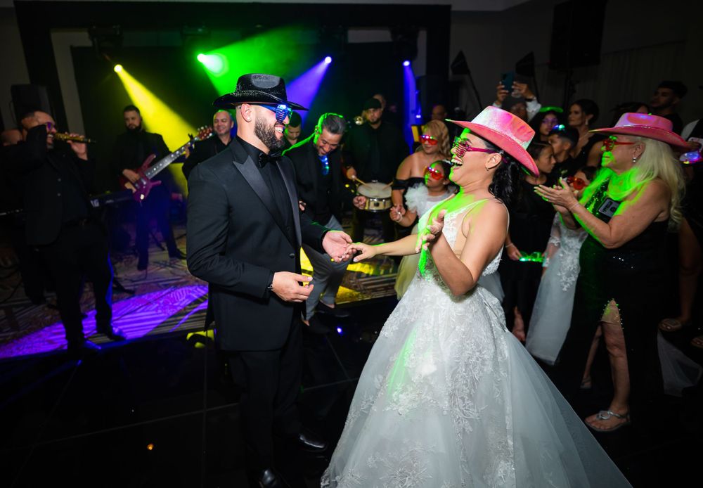 Wedding party guests wearing pink cowboy hats dance under colorful disco lights.