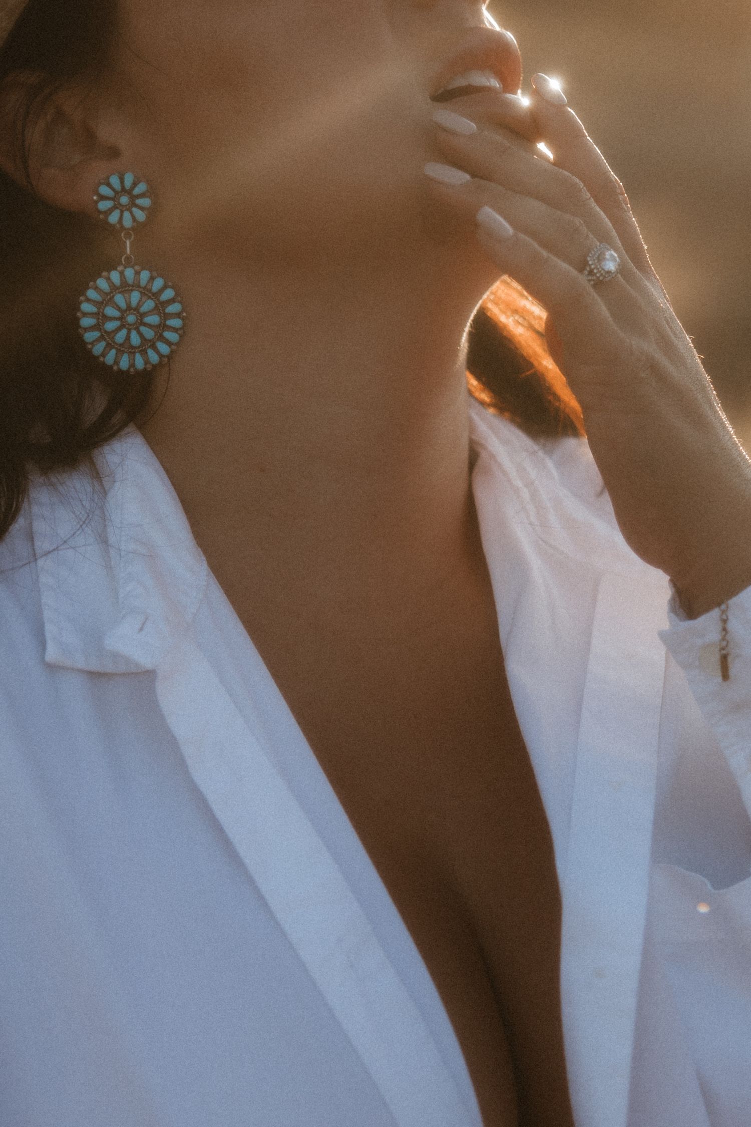 A close-up shot shows turquoise statement earrings against a white blouse in warm sunlight.