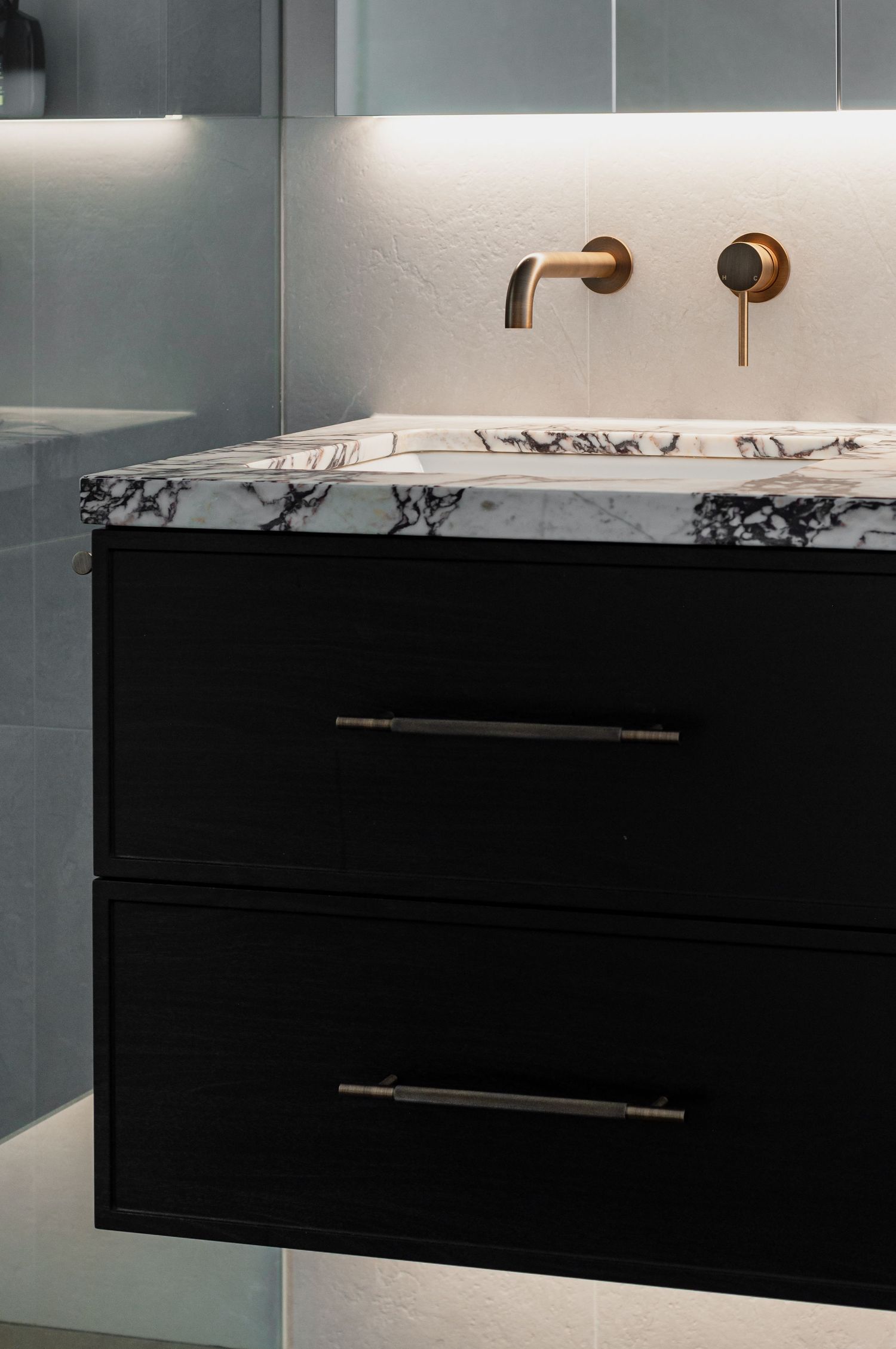 Modern bathroom vanity with black drawers and marble countertop featuring wall-mounted brass faucets.