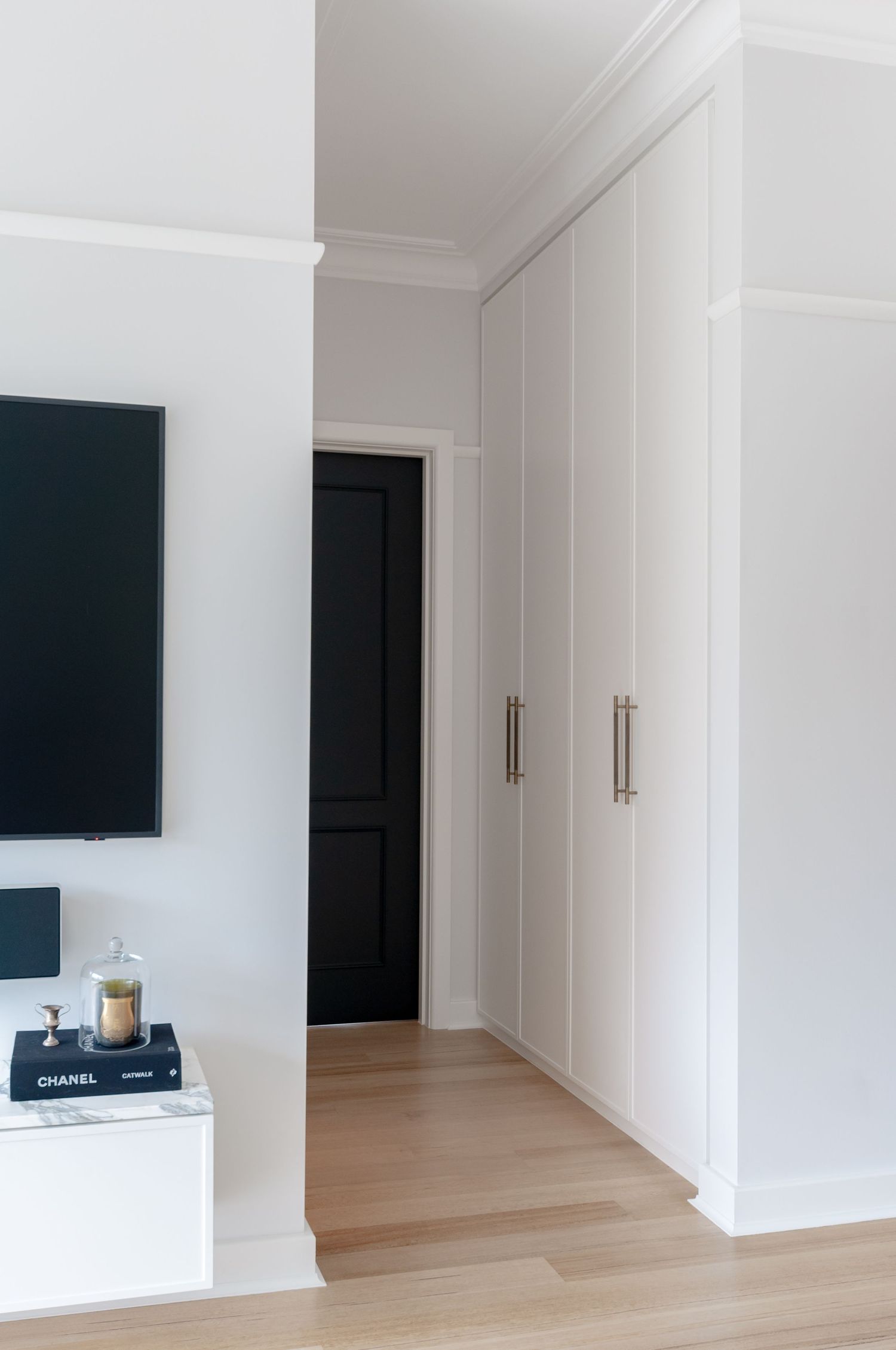Minimalist hallway with white built-in closets, black door, and hardwood flooring.