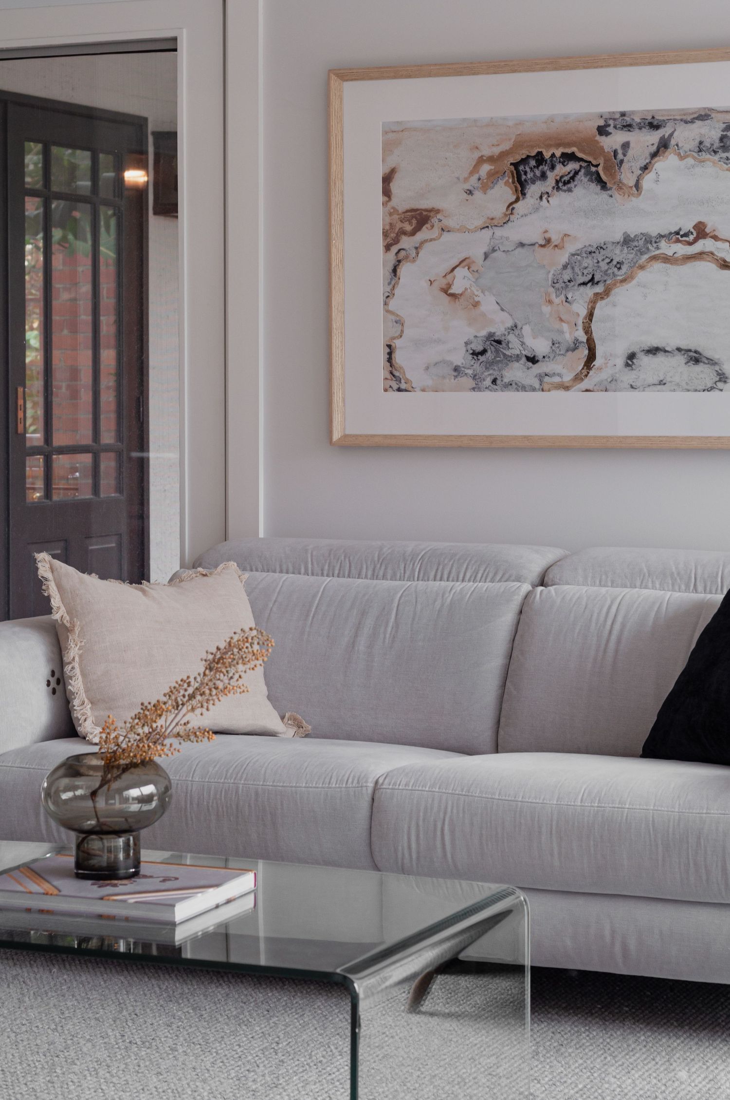 Contemporary living room with marble art print, grey sofa, and glass coffee table.
