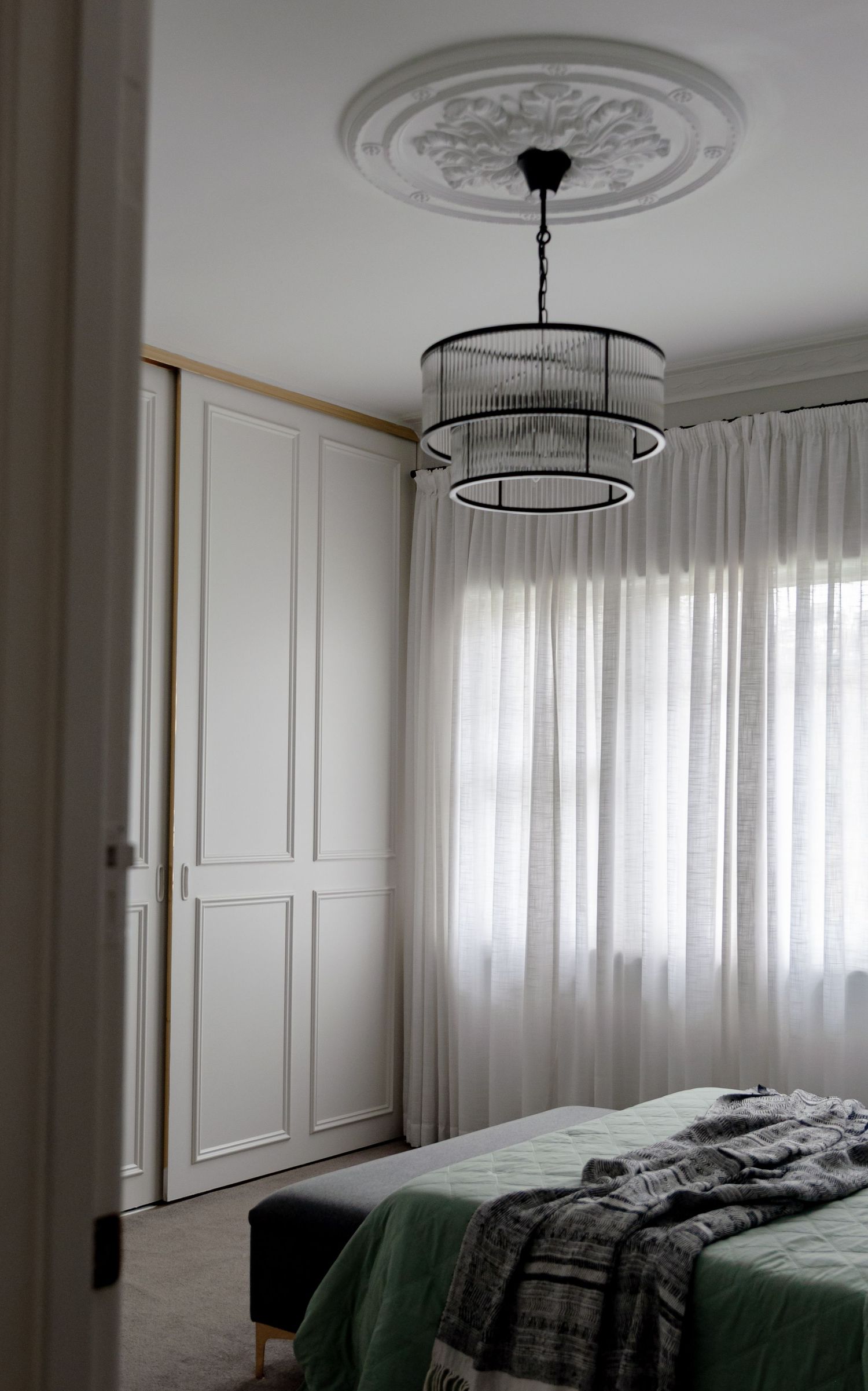 Elegant bedroom with tiered chandelier, ornate ceiling medallion, and white built-in wardrobe.