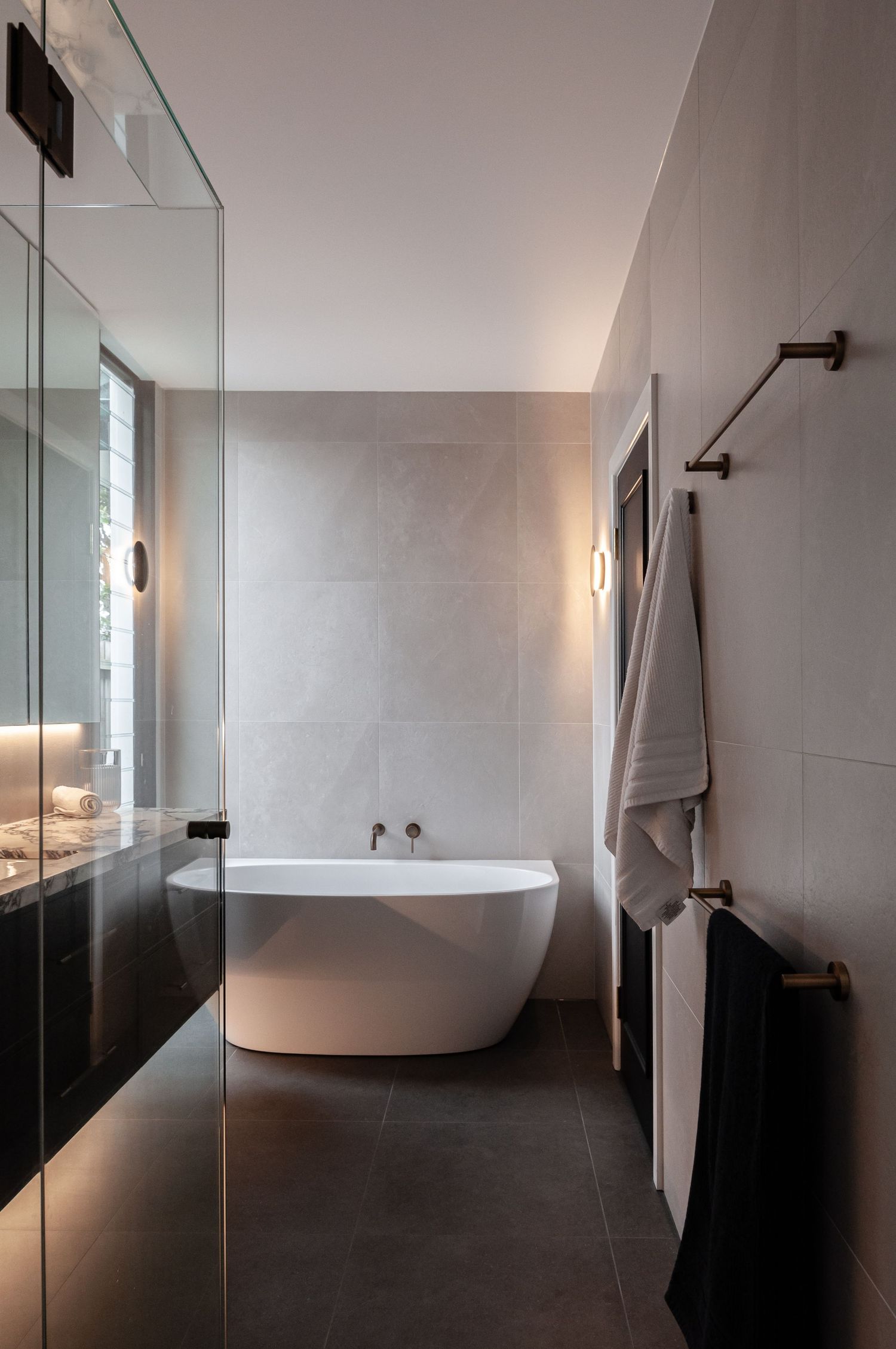 Minimalist bathroom with freestanding white tub and dark floor tiles illuminated by soft lighting.