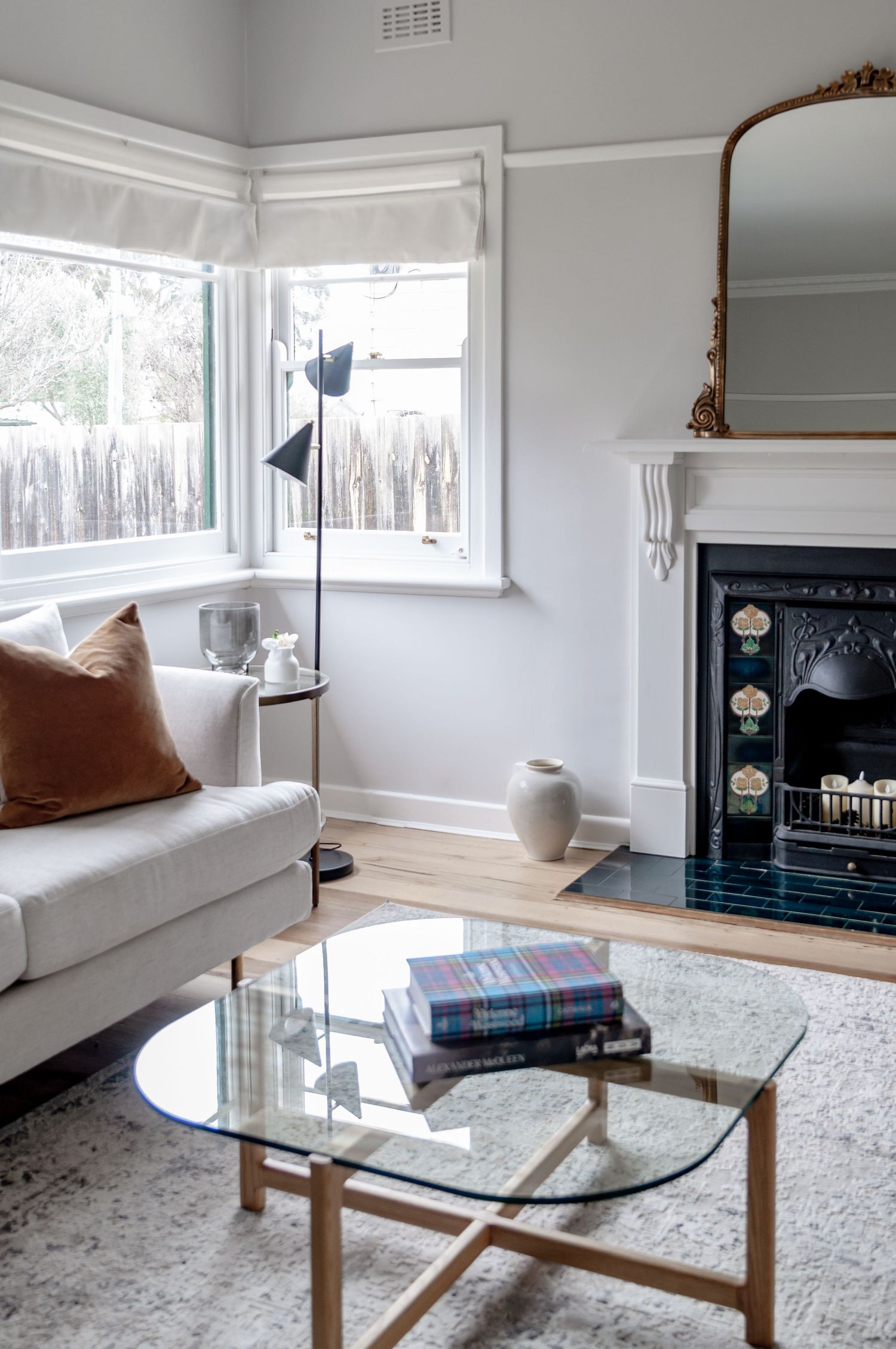 Bright living room with bay window, glass coffee table, and decorative fireplace.